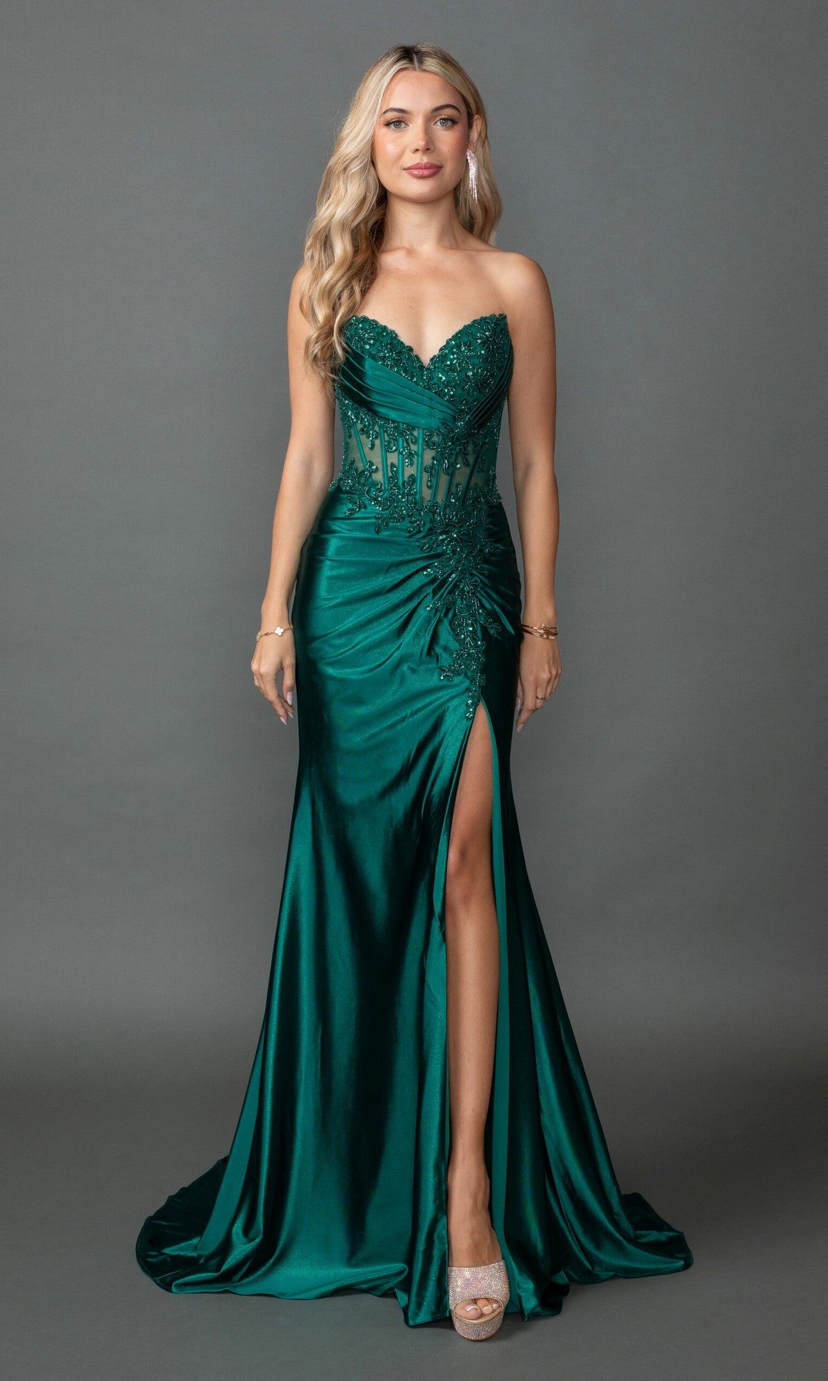 A woman models the Dancing Queen 4560 long prom dress, featuring a strapless dark green design with a sweetheart neckline, beaded lace corset, thigh-high slit, and floor-length skirt against a plain gray background.